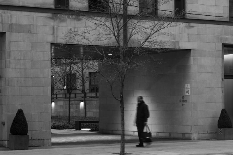 A man walking down the street, illuminated by a spot of sunlight